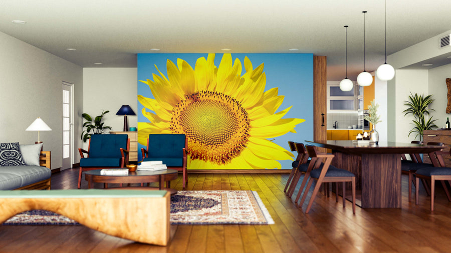A modern open-plan living and dining area with wood floors, blue chairs, contemporary lighting, a dining set, rugs, and decor features the Radiant Sunflower Wall Mural on a blue wall, creating a bright and inviting space.
