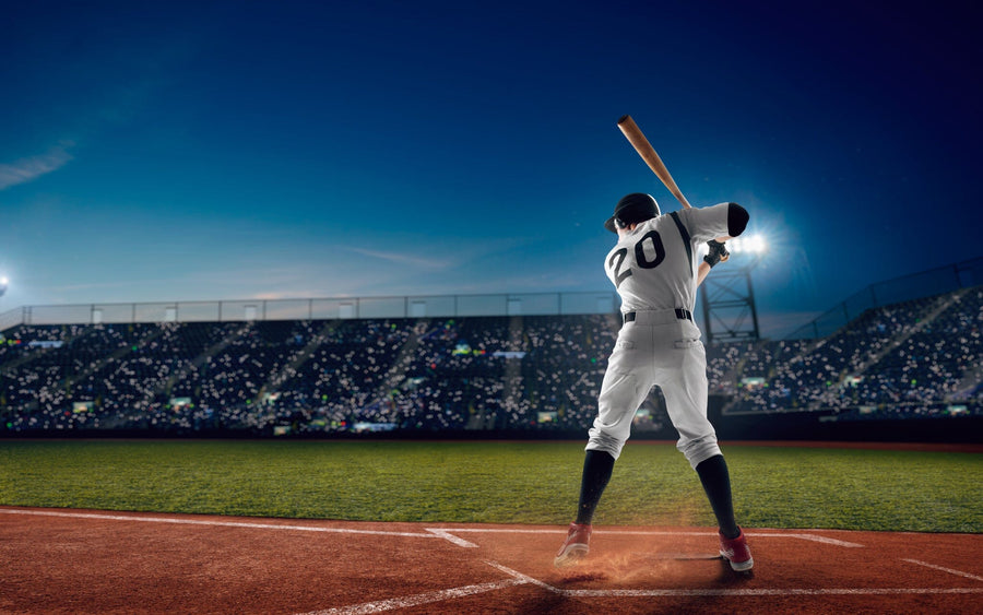 A bedroom features the Ready to Swing Wall Mural showing a baseball player at bat in a night stadium, plus a bed, desk, chair, sports decor, light wood floors, natural light, and a soccer ball near the bed.