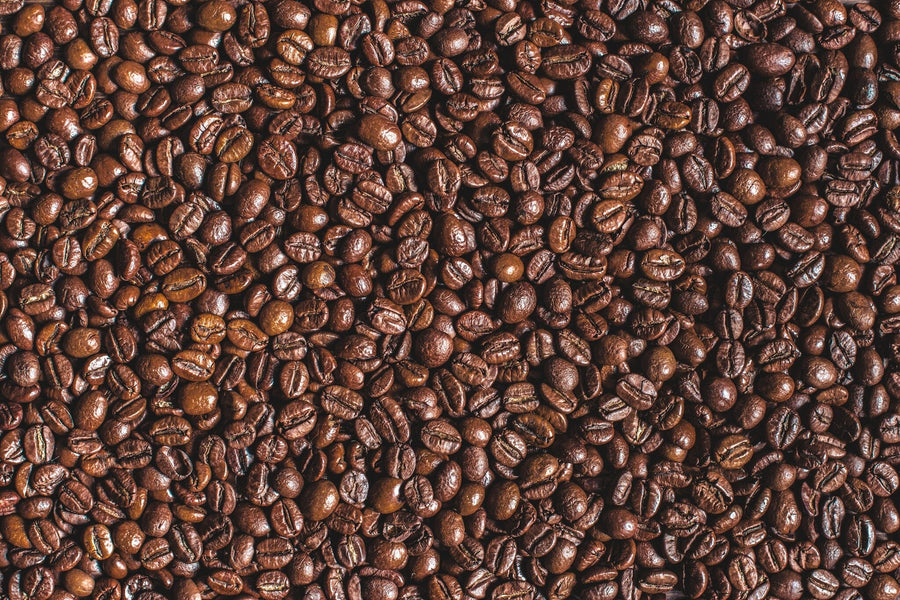 A modern café features wooden tables, stools, and small potted plants. The "Rich and Aromatic Wall Mural" showcases a close-up of glossy coffee beans. Pendant lights hang overhead, while large windows fill the space with natural light.