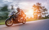 A motorcyclist in black gear zooms down a road on a sleek bike, framed by the warm glow of sunset and blurred trees, much like the Riding into the Sunset Wall Mural that brings the thrill of open roads to your walls.