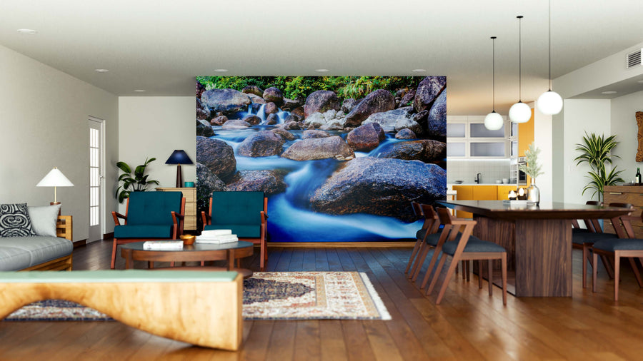 A modern open-plan living and dining room features wood floors, contemporary furniture, and a large River Stones Wall Mural of a flowing rocky stream. Natural light brightens the cozy seating area and wooden dining table with chairs.