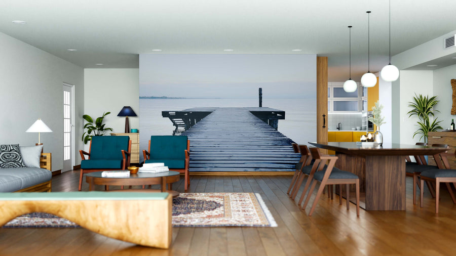 A modern living-dining room features wooden floors, teal armchairs, and a gray sofa. The Serene Wooden Dock Wall Mural adds depth, while plants, pendant lights, and eclectic decor create a cozy, stylish atmosphere.