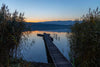 The Silent Lake Wall Mural captures a wooden dock reaching into a tranquil lake at sunset, with rowboats and glowing skies—bringing peaceful beauty to your space as a stunning custom mural or removable wallpaper.
