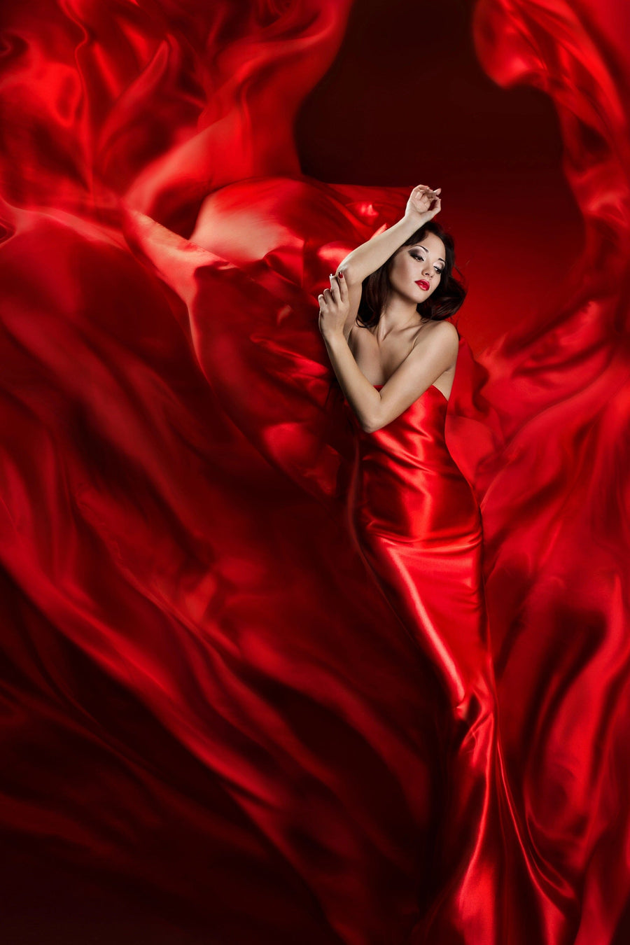 A woman in a flowing red dress poses gracefully, her dark hair elegantly styled and lips painted red. Surrounded by swirling fabric resembling the Silk Embrace Wall Mural, the background blends with the dynamic design, creating a captivating scene akin to removable wallpaper art.