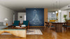 Modern open-concept living and dining area with wood floors, teal chairs, a wooden coffee table, and a large Sitting Buddha Over Blackboard Background Wall Mural on a dark blue accent wall. Dining area includes a long wooden table, pendant lights, and kitchen views.