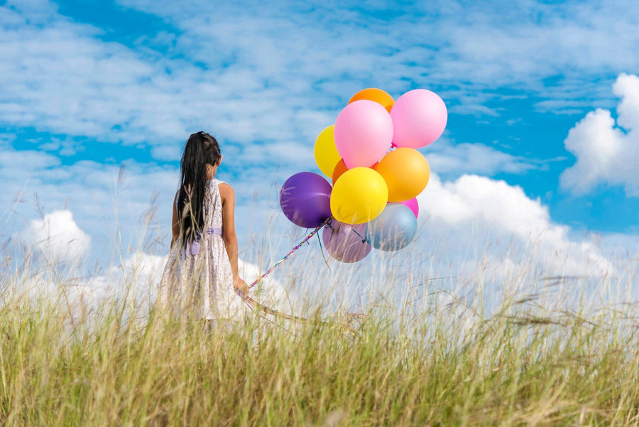 A modern living-dining room with wooden floors and contemporary furniture features the Skybound Dreams Wall Mural—a vibrant image of a woman holding colorful balloons in a grassy field—adding a whimsical focal point to the space.