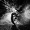 The Smoke Wall Mural by Photo features a black-and-white image of a motorcycle rider enveloped in fog. A low-angle view highlights the front wheel and dynamic spokes, while intense light beams pierce the mist, creating a dramatic and mysterious silhouette.