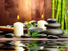 The photo Spa Wall Mural creates a tranquil spa scene with lit white candles, smooth black stones on a bamboo mat, and green bamboo stalks reflected in the water below.