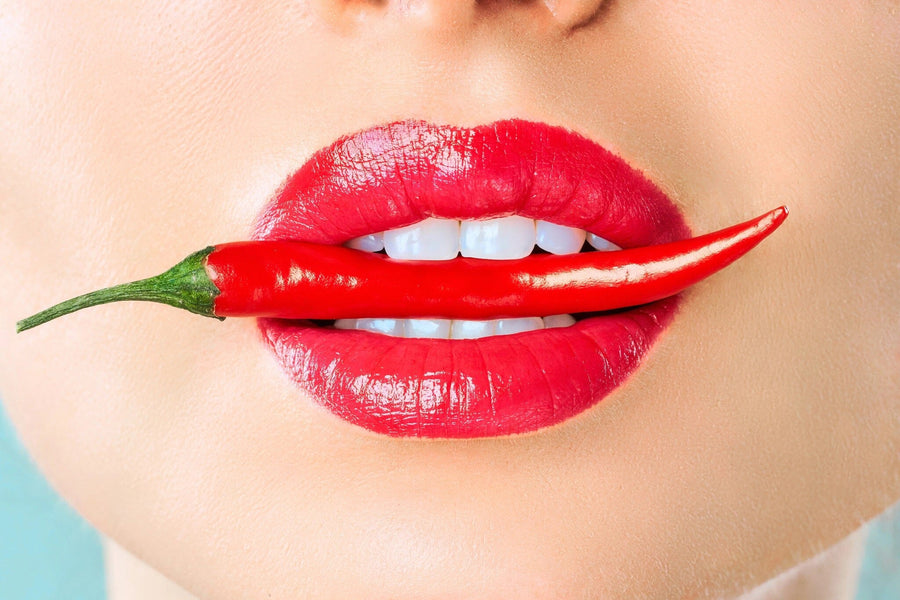 A close-up of glossy red lips gently biting a chili pepper stands out in the Spicy Lips Wall Mural, with bold lipstick and smooth skin adding fiery style to any peel and stick mural backdrop.