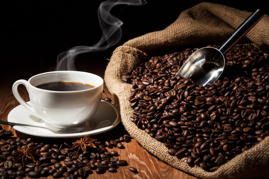 A cozy café with wooden tables and stools, potted plants, large left-side windows, and a Steaming Hot Coffee Wall Mural showing a steaming cup, burlap sack of coffee beans, and a metal scoop.