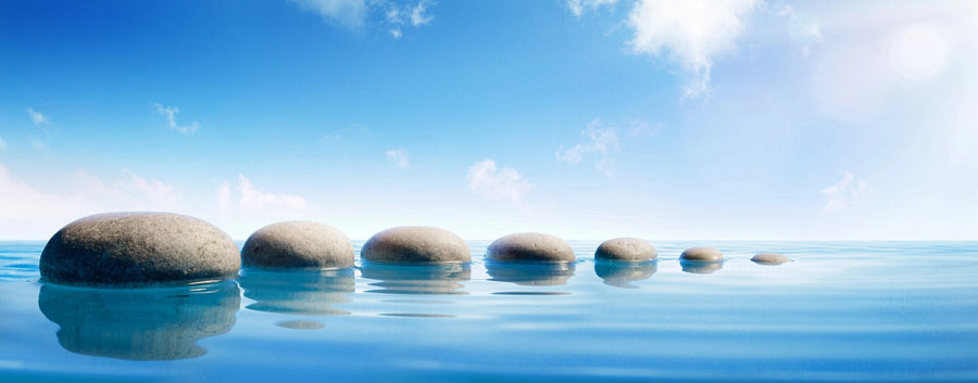 Modern open living and dining area with wood floors, stylish furniture, pendant lights, and the Step Stones In Blue Water Wall Mural as a serene, nature-inspired focal point featuring smooth stone balls in calm water against a bright blue sky.