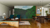 A modern living and dining room with wooden floors, green armchairs, a wood table, pendant lights, rugs, decor items, and the Sugba Lagoon Wall Mural of a lush forest and river creates a warm, cozy atmosphere.