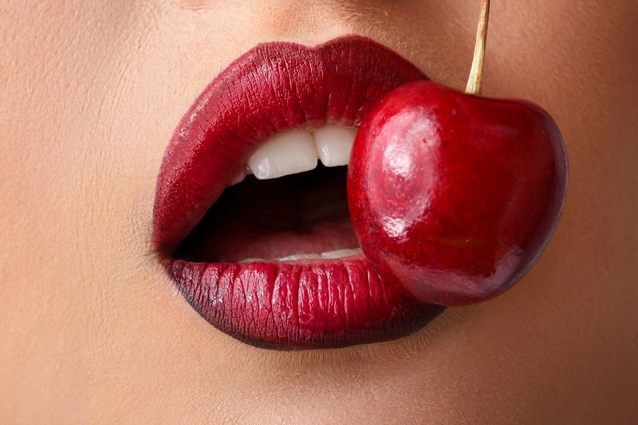 A close-up features lips in dark red lipstick, teeth slightly showing, with a cherry near the mouth—highlighting the glossy effect of the Sultry Cherry Bite Wall Mural against a blurred background.