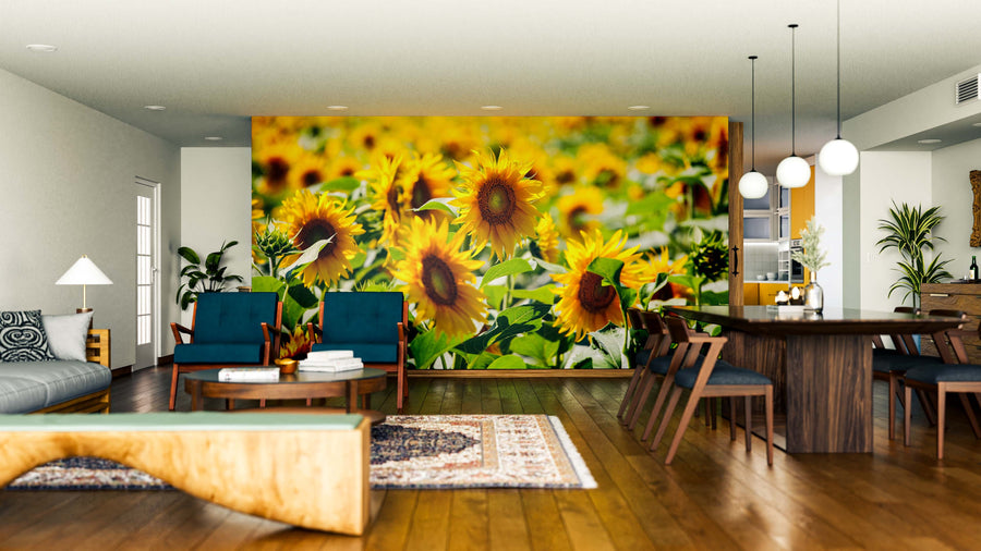 A modern living-dining room with wood floors, mid-century furniture, and a large Summer Blossoms Wall Mural featuring sunflowers. Plants, pendant lights, and teal accents complete the warm, inviting atmosphere.