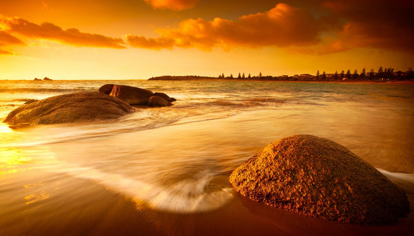 A serene sun tinted beach with rocks and water – Peel and Stick Wall Murals
