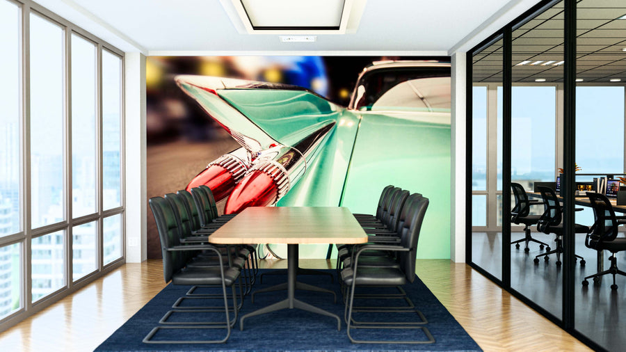 A modern conference room with a long table, black chairs, and glass walls features the Sunday Driver Wall Mural, showcasing a classic green car’s tail fin and red tail lights. Sunlight from the windows brightens the space.