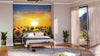 A bright bedroom features the Sundown on Sunflower Field Wall Mural behind the bed, which is dressed in white and gray bedding. Nightstands with plants flank each side, sunlight pours in, and a wooden bench rests at the foot of the bed.