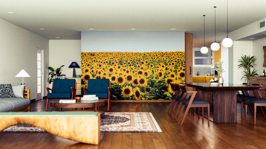A modern open-plan living and dining room features wood floors, stylish furniture, potted plants, and the Sunflower Bloom Horizon Wall Mural, showcasing a vibrant sunflower field under a blue sky as a lively focal point.