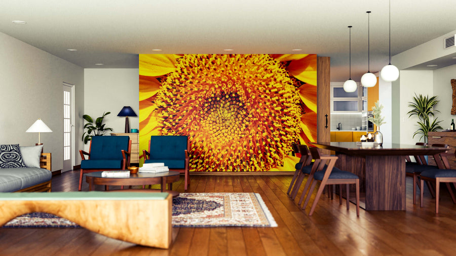 A modern open-plan living-dining space features wooden floors, mid-century furniture, and a Sunflower Close-Up Wall Mural. Blue chairs, a wooden dining table, plants, pendant lights, and rugs create a warm, inviting feel.