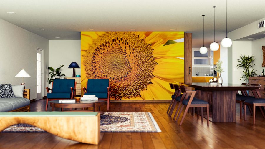 A modern open-concept living and dining area features wooden floors, blue armchairs, and the Sunflower Closeup Wall Mural. Pendant lights hang above a dark dining table, with plants and contemporary furniture completing the space.