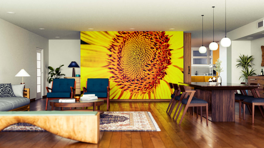 A modern living-dining room features wood floors, blue chairs, a gray sofa, and a large Sunflower Core Wall Mural. A long dining table with wooden chairs sits under globe lights, with the kitchen visible in the background.