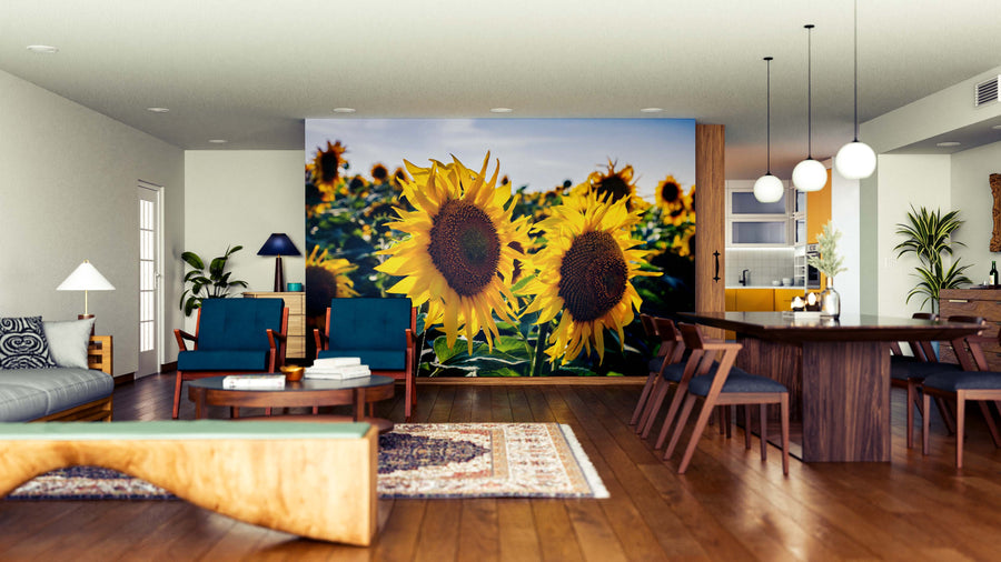 A modern open-plan living and dining area features wooden floors, blue armchairs, the Sunflower Duo Wall Mural, round pendant lights, indoor plants, and a blend of contemporary and rustic furniture for a bright and inviting space.