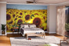 A cozy bedroom featuring the Sunflower Field Close up Wall Mural behind the bed, wooden furniture, a gray rug, two potted plants, a ceiling fan, and sunlight filtering through sheer curtains on sliding glass doors to a balcony.