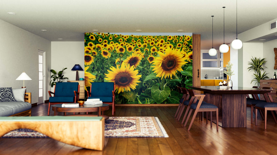 A modern open-concept living and dining area features a bold Sunflower Harmony Wall Mural. Wooden floors, blue-upholstered furniture, pendant lights, plants, and cozy accents complete the inviting space.