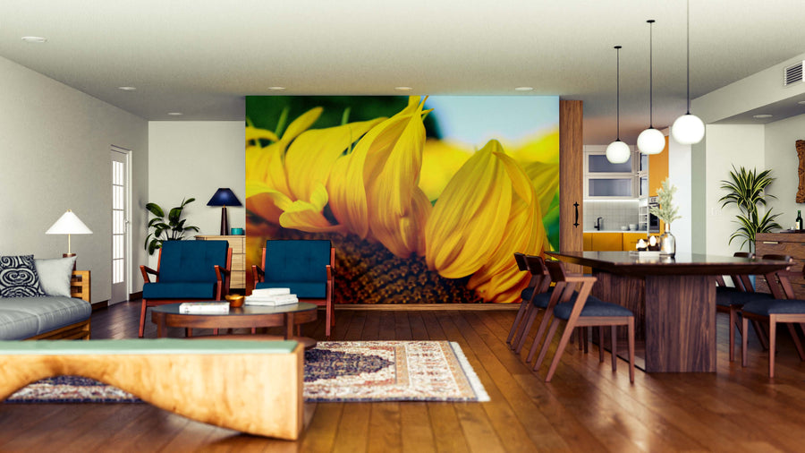 A modern open-plan living and dining room showcases wooden floors, blue chairs, a large dining table, eclectic decor, rugs, pendant lights, and natural light, highlighted by the Sunflower Petals Wall Mural on the back wall.
