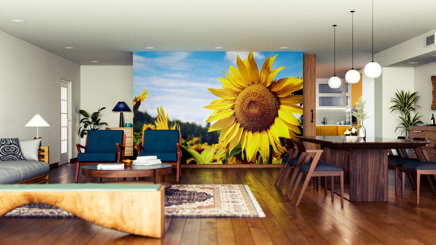 A modern living-dining room features wooden furniture, blue chairs, and the Sunflower against a Blue Sky Wall Mural, creating a bright, inviting vibe. Rugs, a sofa, and pendant lights complete this stylish, welcoming space.