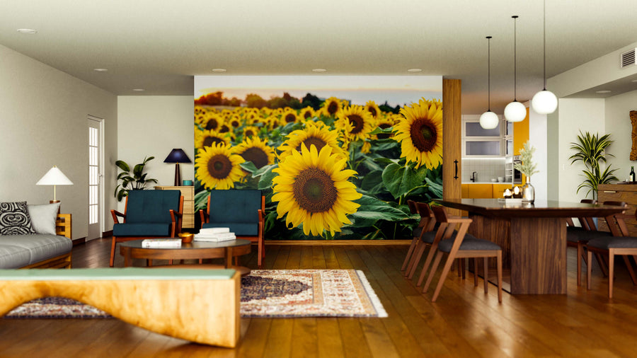 A modern living and dining room with wooden floors and furniture features the Sunflowers at Sunset Wall Mural on the back wall, adding vibrant color and warmth. Pendant lights hang above the dining table, while rugs accent the seating area.