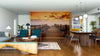 A modern open-plan living and dining room features wooden furniture, blue chairs, and pendant lights. The "Sunset Beach in Gabo de Gata Wall Mural" adds warmth and depth, while rugs and decor complete the cozy atmosphere.