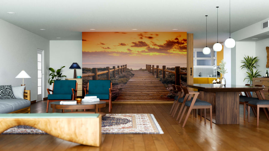 A modern open-plan living and dining room features wooden furniture, blue chairs, and pendant lights. The "Sunset Beach in Gabo de Gata Wall Mural" adds warmth and depth, while rugs and decor complete the cozy atmosphere.