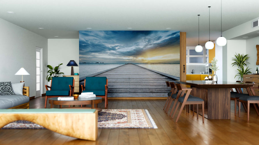 A modern living and dining area with wooden furniture features the "Sunset Beach in Koh Samui Wall Mural." Teal chairs, a rug, potted plants, and pendant lights complete this inviting space.