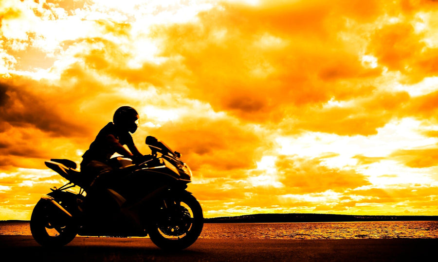 A modern garage with black cabinets, organized tools, and two motorcycles features the Sunset Chase Wall Mural—a striking image of a rider against a sunset sky—revealed through the open door as sunlight brightens the polished space.