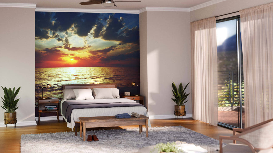 A modern open-plan living and dining room with wood floors, teal armchairs, and a kitchen features the Sunset Over Sea Wall Mural, whose vibrant ocean sunset with clouds adds warmth and color to the decor.