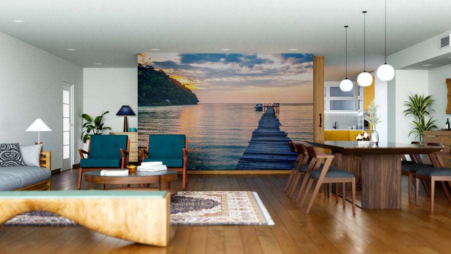 Modern living-dining room with wooden floors, teal chairs, a sofa, and the Sunset Over the Sea Wall Mural featuring a dock at sunset. Contemporary lighting and decor complete this stylish space.