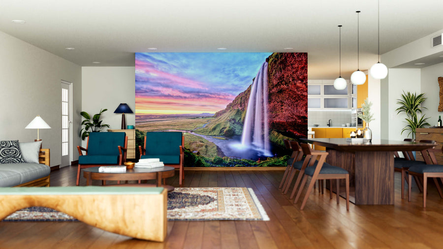 A spacious, modern living and dining area with wood floors and mid-century furniture is brightened by the Sunset at Seljalandfoss Waterfall Wall Mural, adding vibrant sunset colors to the neutral interior as a striking focal point.