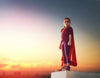 A young girl, embodying the essence of Deposit photo's "Superhero Wall Mural," stands confidently on a rooftop at sunset. Wearing a red cape, purple mask, matching outfit, and sneakers, she clenches her fist proudly while gazing toward the horizon like a living superhero.