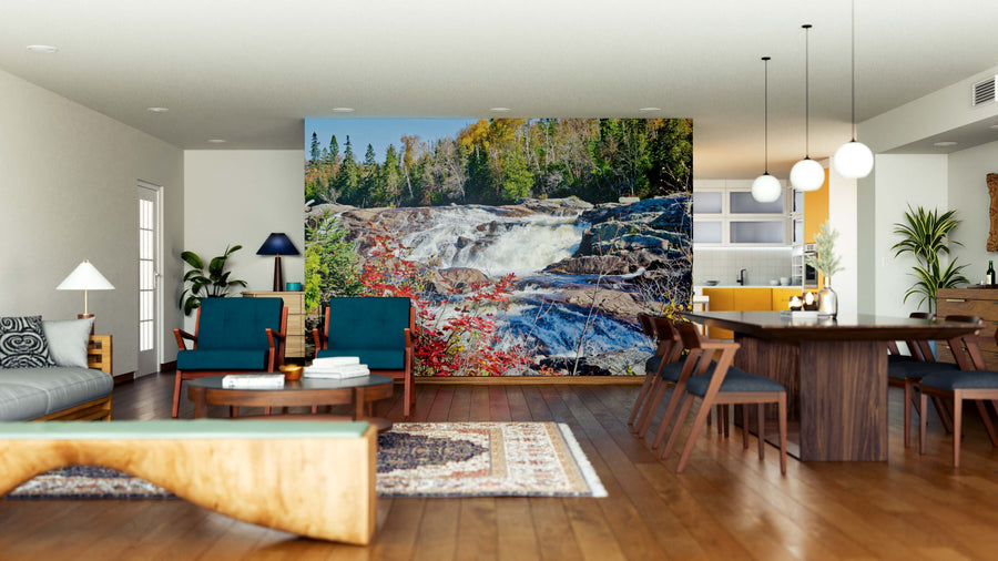 A modern, open living-dining room showcases wood floors, stylish furniture, and a Superior Lake Provincia Wall Mural of a waterfall in an autumn forest as the focal point, enhanced by bright lighting and a cozy atmosphere.