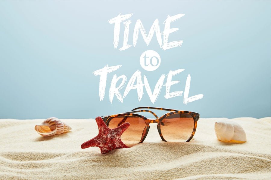 A modern living-dining area with wood floors, blue armchairs, and a dining set is brightened by the Time to Travel Wall Mural, featuring sunglasses and sand for a beachy, vacation vibe.