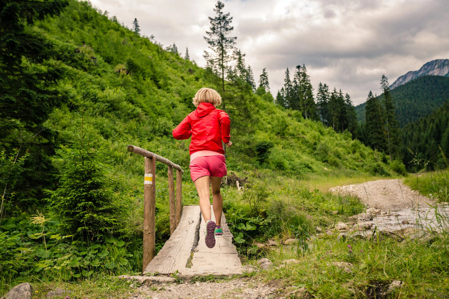 A modern living and dining room features wood furniture, a cozy sitting area, and the Trail Running Wall Mural showing a person in a red jacket running on a forest path with mountains in the background.