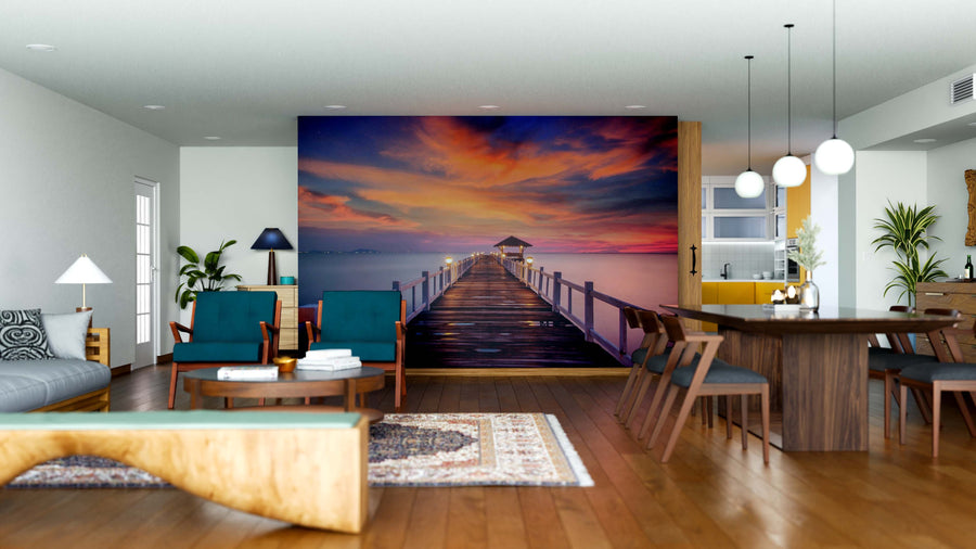 A modern living and dining area features wooden floors, contemporary furniture, and the Tranquil Twilight Dock Wall Mural depicting a sunset pier over calm water. Pendant lights illuminate a dark dining table to the right, creating a vibrant focal point.