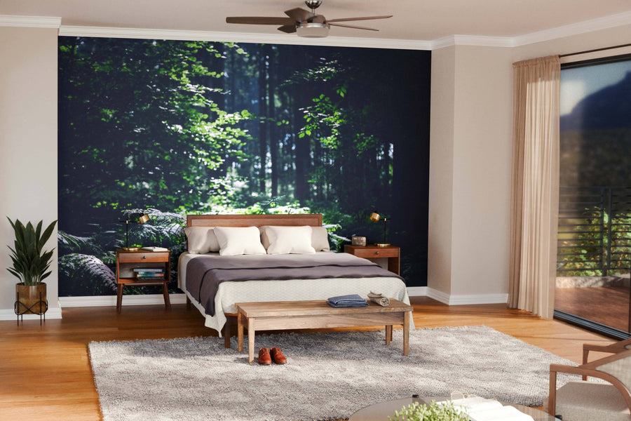 A cozy bedroom features a large Trees in Beautiful Forest Wall Mural behind a wooden bed with white and beige bedding. Two wooden nightstands with lamps flank the bed, while large windows let in natural light.