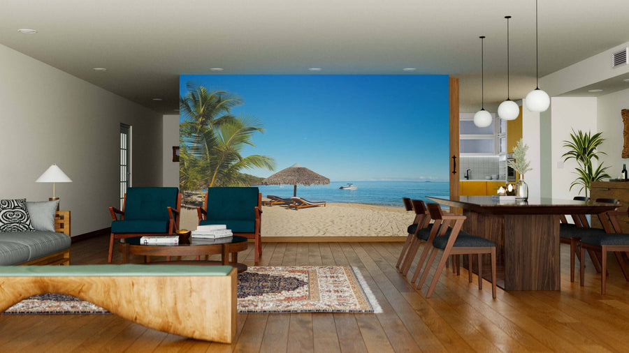 A modern living-dining room features wood furniture, area rugs, and pendant lights. The Tropical Beach Panorama Wall Mural with palm trees and lounge chairs adds a relaxing, seaside-inspired vibe to the space.