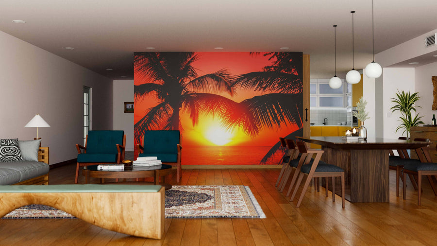 A modern living and dining room with wooden floors and furniture features the Tropical Beach Sunset Wall Mural, showing a vivid tropical sunset with palm trees. Contemporary lighting and rugs complete the stylish, warm decor.