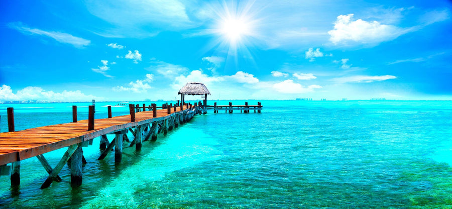 Modern living and dining area with wood floors and mid-century furniture; the Tropical Horizon Wall Mural features a vivid tropical pier extending into turquoise water under a sunny sky, creating an ocean view illusion indoors.