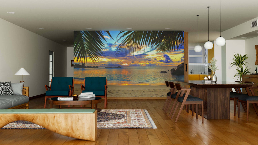A modern living-dining room with wood floors and contemporary furniture features the Tropical Beach at Sunset Wall Mural, showcasing palm leaves and ocean views for a vibrant, relaxing feel. Pendant lights hang above the dining table.