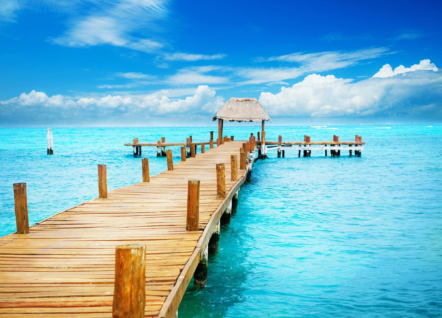 A modern open-concept living and dining room features wooden furniture, blue chairs, and the "Vacation in Tropic Paradise Wall Mural," showcasing a pier over turquoise water under a sunny sky for a serene coastal vibe.