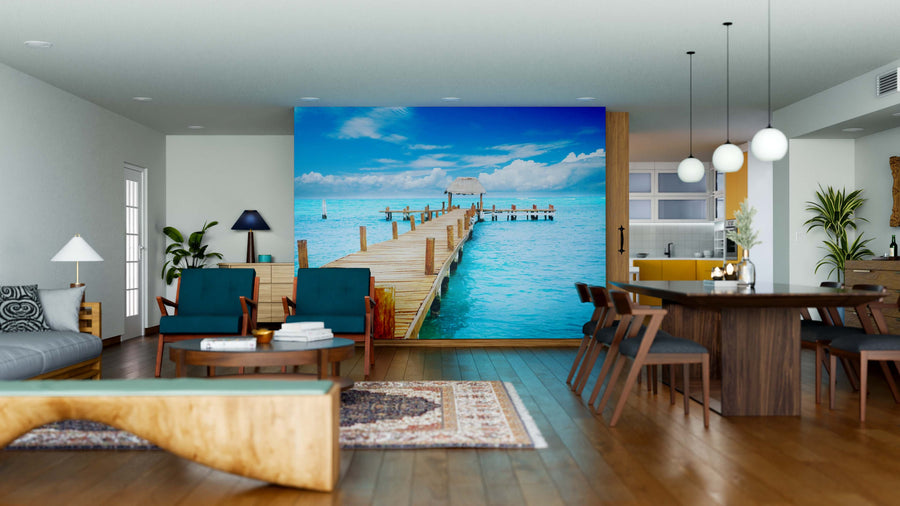 A modern open-concept living and dining room features wooden furniture, blue chairs, and the "Vacation in Tropic Paradise Wall Mural," showcasing a pier over turquoise water under a sunny sky for a serene coastal vibe.